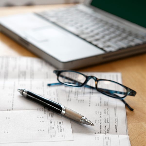 dator, glasägon, papper och penna ligger på ett skrivbord