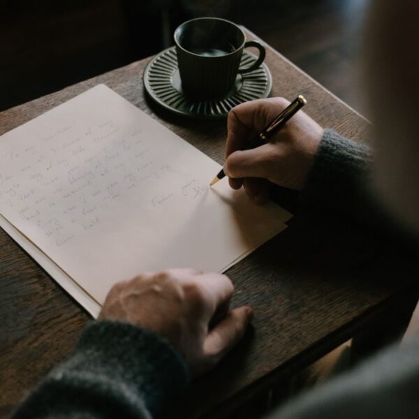 En person skriver testamente vid ett bord med en kaffekopp på.