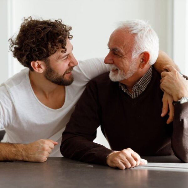 En medelålders man sitter bredvid en äldre man och håller om honom med ena armen.