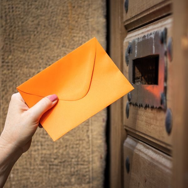 En hand som postar ett oranget kuvert till Skatteverket.